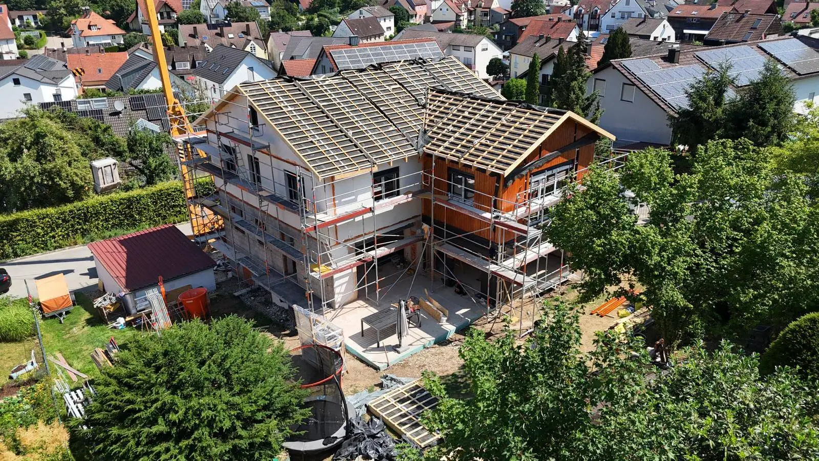 Aerial view of the construction site: new roof structure with battens, timber façade on the extension, scaffolding all around